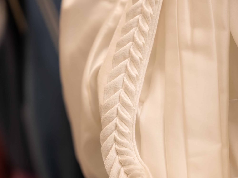 Detail eines cremefarbenen Brautdirndls mit gestiftelter Federkiel-Verzierung aus dem Maßatelier der Sportalm Waltner