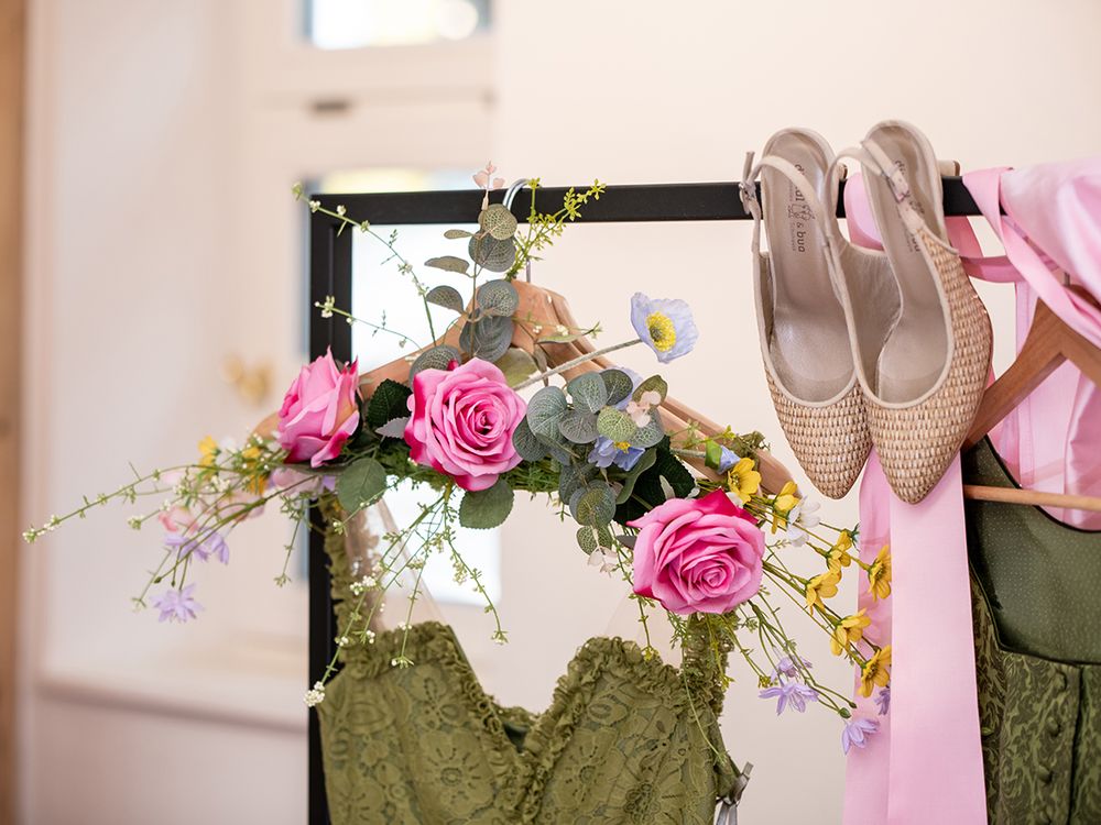 Grünes Spitzendirndl mit Blumenschmuck und Brautschuhen am Kleiderständer der Sportalm Waltner in Nesselwang