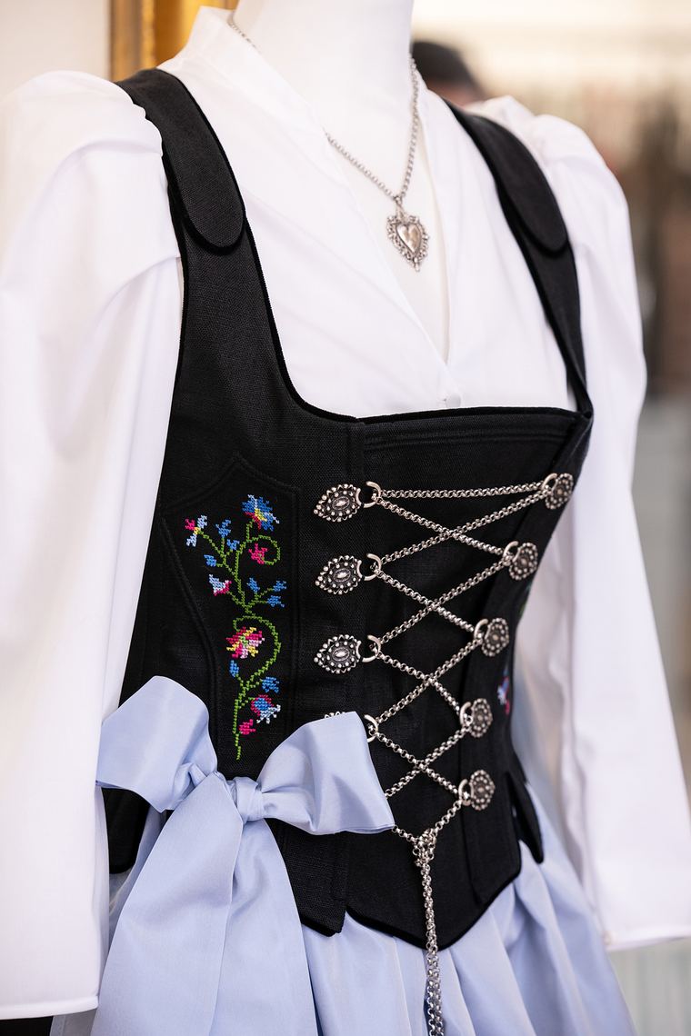 Schwarzes Trachtenmieder mit bunter Kreuzstich-Blumenstickerei, Silberschnürung und hellblauer Schleife aus dem Maßatelier der Sportalm Waltner