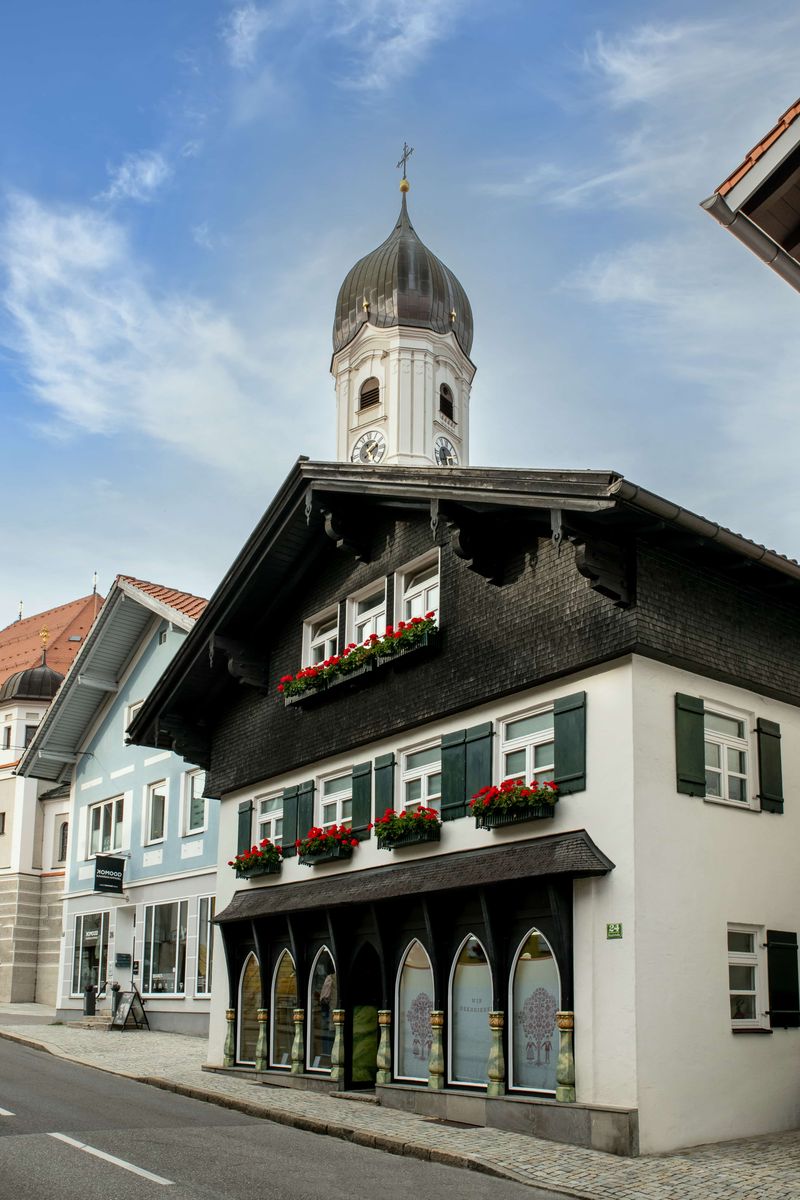 Das Trachtenhaus Sportalm Waltner an der Hauptstraße 24 in Nesselwang mit dem Zwiebelturm der Kirche St. Andreas im Hintergrund