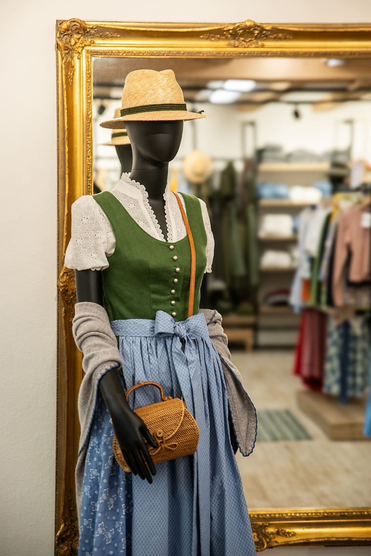 Grünes Leinen-Dirndl mit weißer Trachtenbluse, blauer Schürze und Strohhut vor dem Goldrahmenspiegel der Sportalm Waltner in Nesselwang